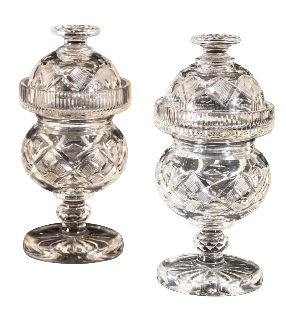 A pair of late 19th-century clear cut glass sweetmeat jars featuring domed lids, diamond-cut facets, knopped stems, and star-cut circular bases.
