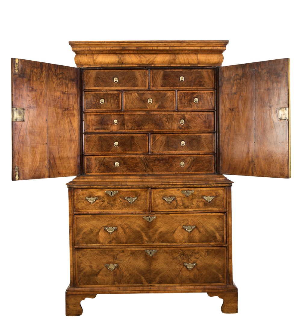 An antique George I walnut cabinet on chest featuring two upper veneered cupboard doors above multiple drawers with brass handles and bracket feet. View II