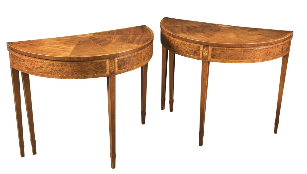 A pair of late eighteenth-century George III mahogany demi-lune card tables featuring fan-shaped veneered tops, inlaid friezes, and square tapered legs.