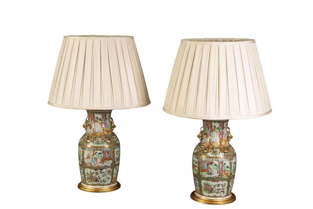 A pair of late 19th-century Cantonese porcelain vase lamps decorated with polychrome figurative panels, mounted on gilt bases with cream pleated shades.