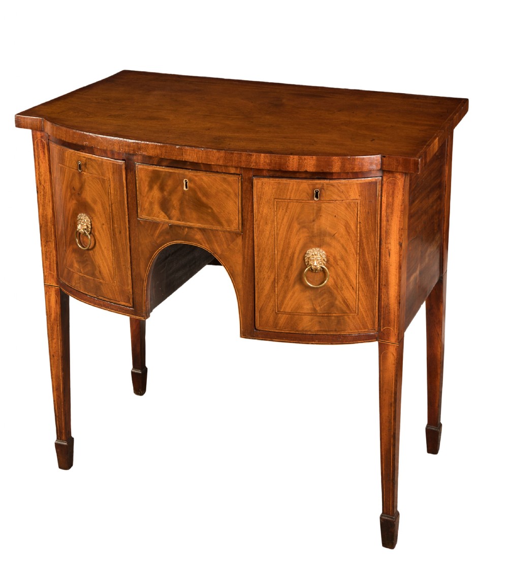 Late eighteenth-century George III mahogany bowfront sideboard with flame mahogany drawers, brass lion mask ring handles, and square tapered legs.
