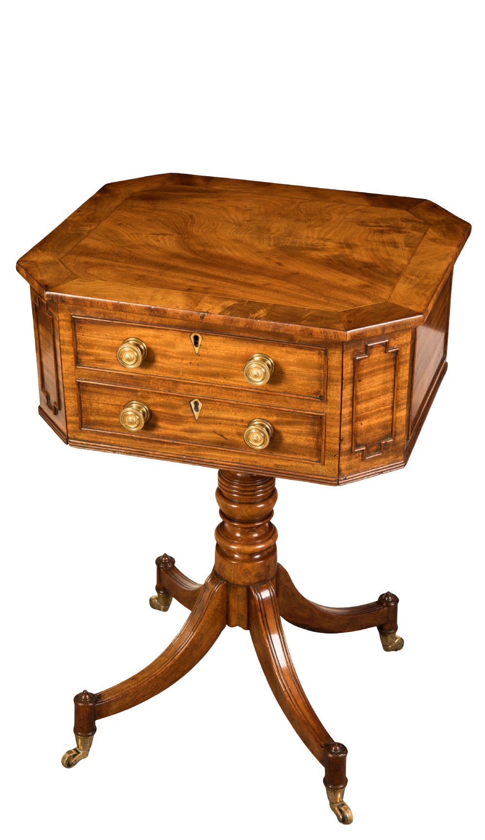 A Regency period mahogany worktable featuring an octagonal canted top, two brass-handled drawers, turned central pedestal, and four splayed legs with brass castors.
