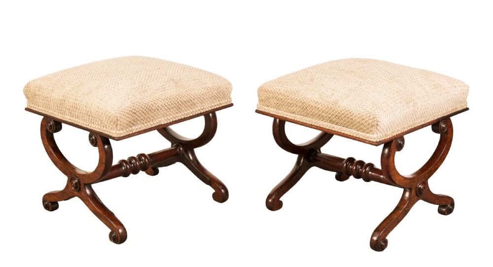 A pair of Regency mahogany X-frame stools featuring woven beige upholstered seats, carved roundels, and turned central stretchers.