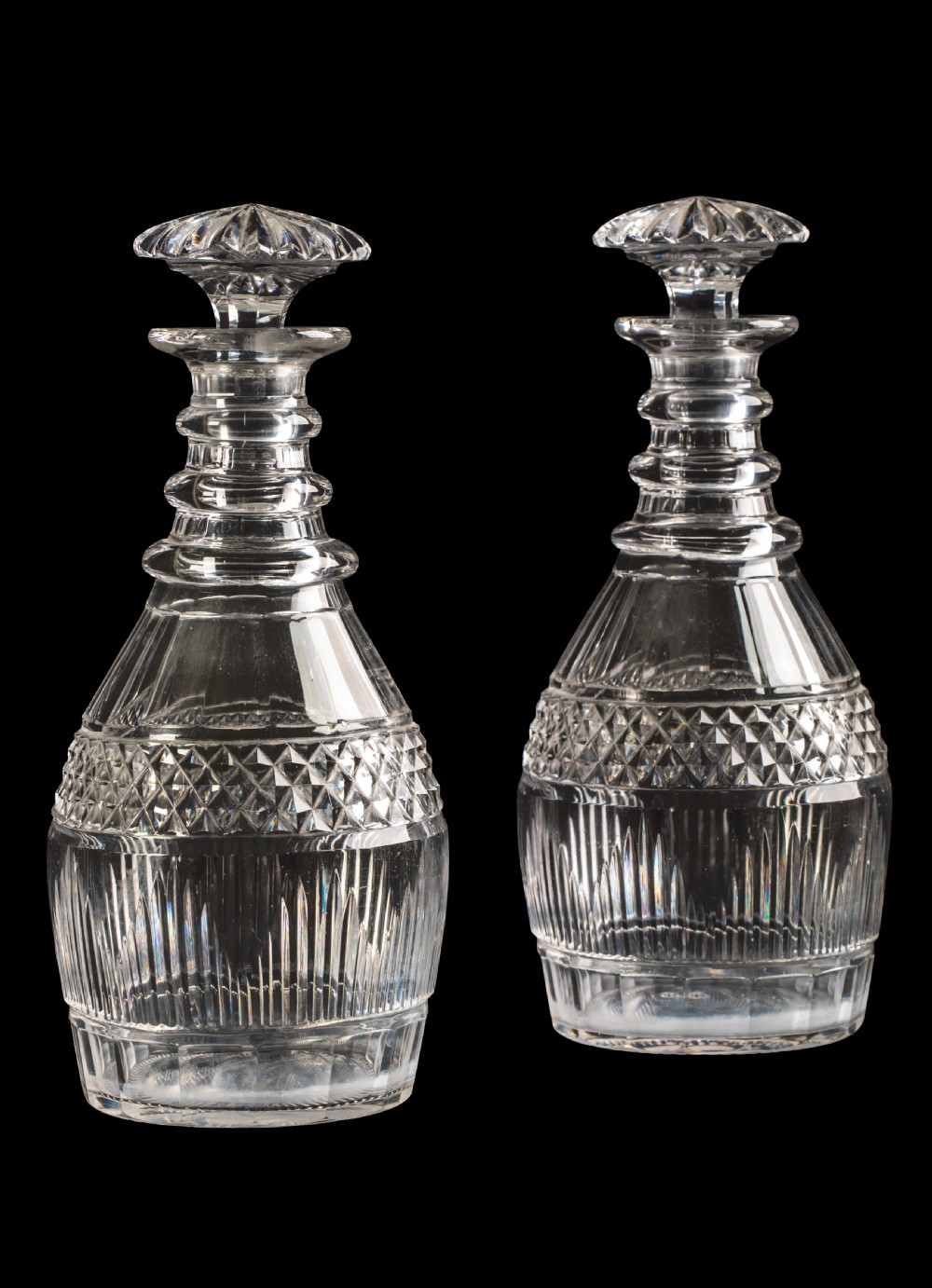 A pair of clear Regency cut glass half-bottle decanters featuring triple neck rings, diamond-cut body bands, and star-cut mushroom stoppers.