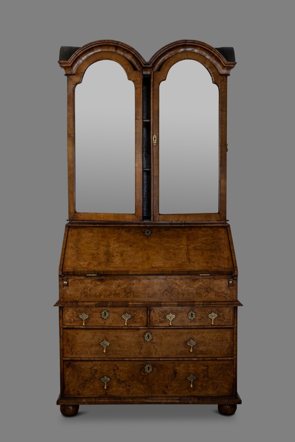 A George I burr walnut bureau bookcase featuring double arched doors with glass panels above a slant-front writing desk and drawers with brass hardware.