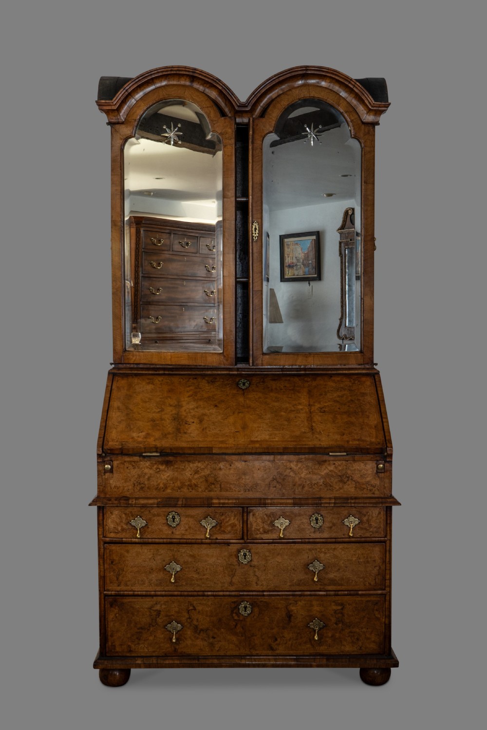 A George I burr walnut bureau bookcase featuring double arched doors with glass panels above a slant-front writing desk and drawers with brass hardware. View II