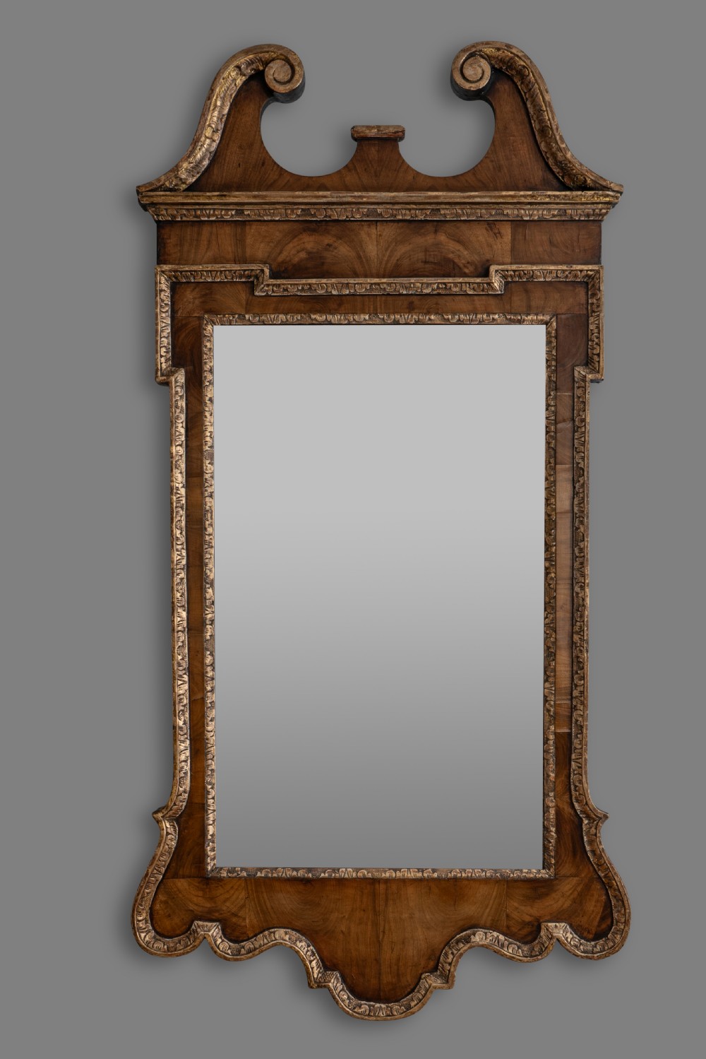 An 18th-century George II walnut wall mirror featuring a scroll-cut pediment, parcel gilt mouldings, and a rectangular mirror plate.