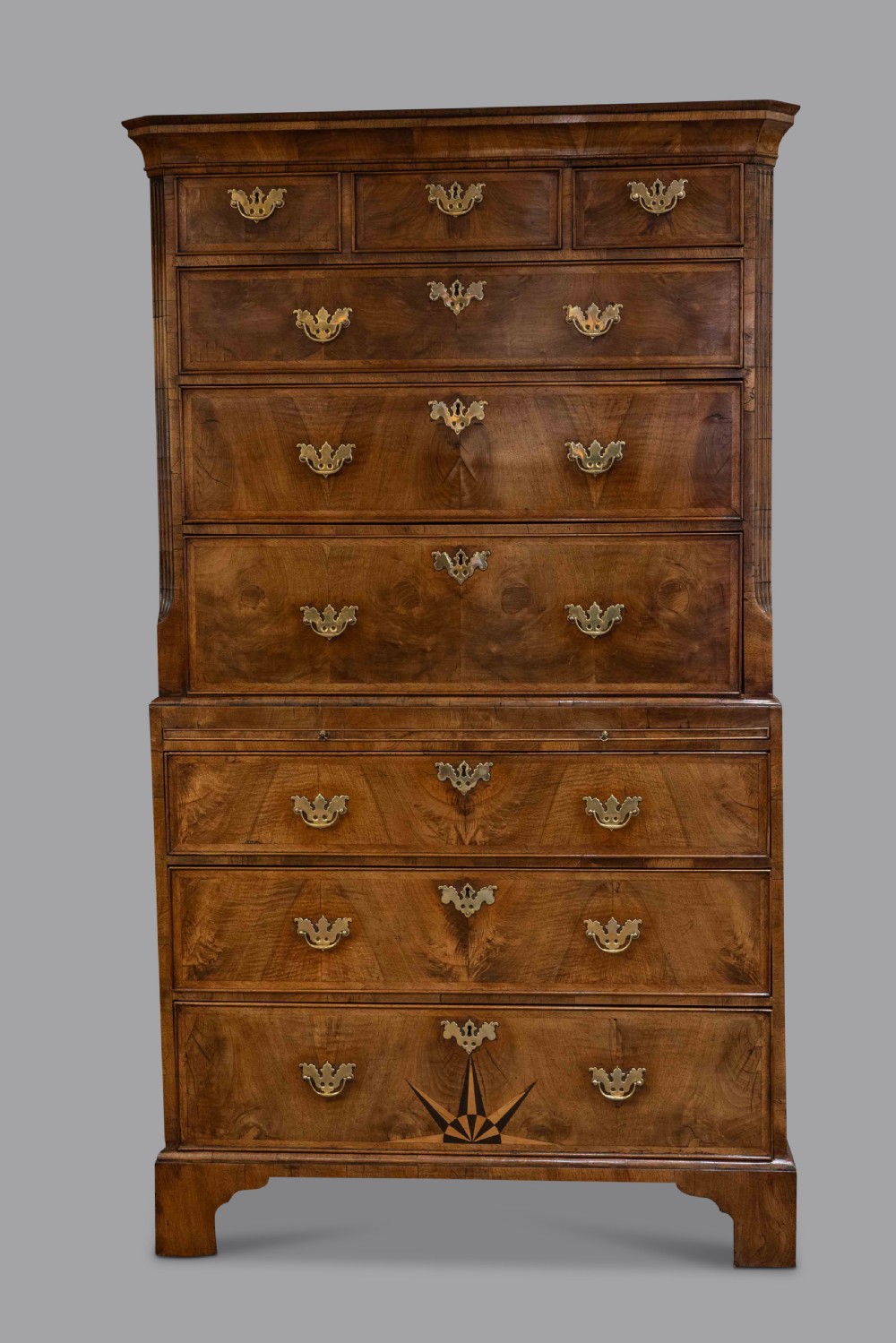A two-section George II walnut chest-on-chest tallboy featuring brass handles, bracket feet, and a starburst inlay design on the lower drawer.