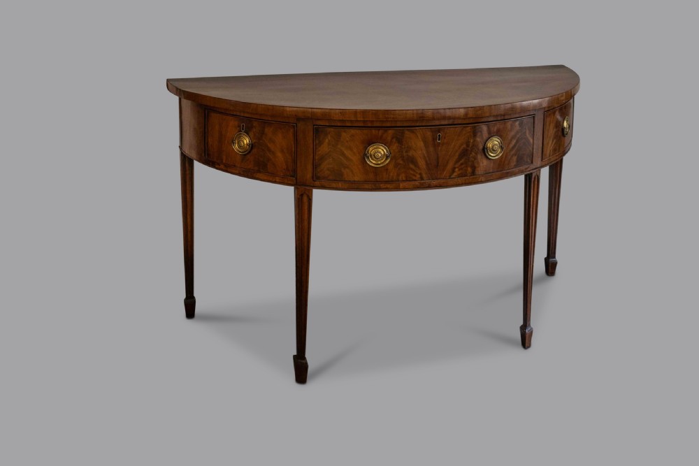 A George III semi-elliptical mahogany side table featuring frieze drawers with brass handles and tapered legs.