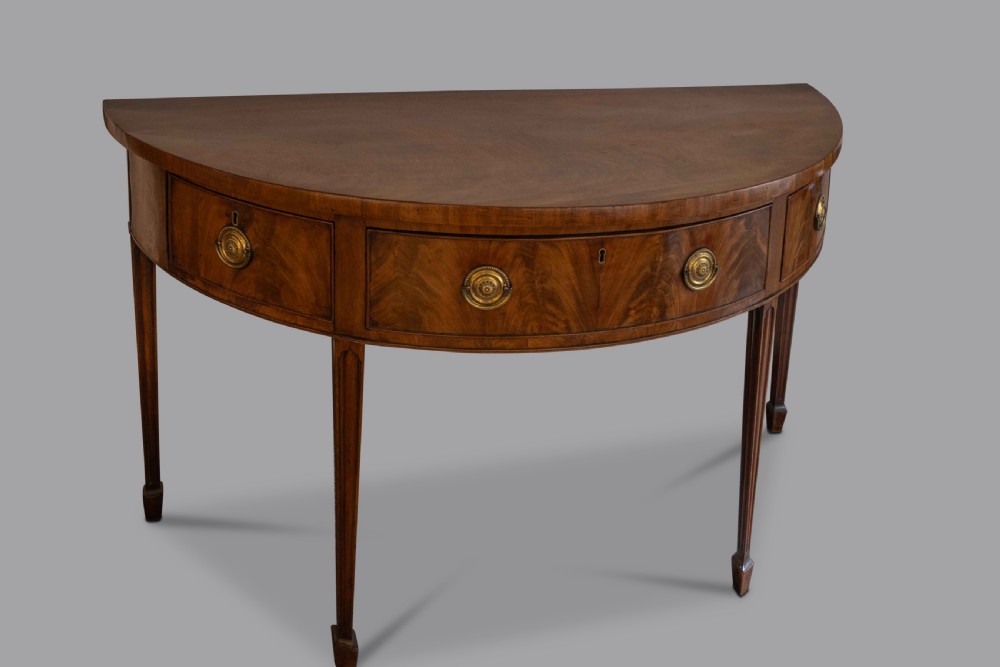 A George III semi-elliptical mahogany side table featuring frieze drawers with brass handles and tapered legs. View II