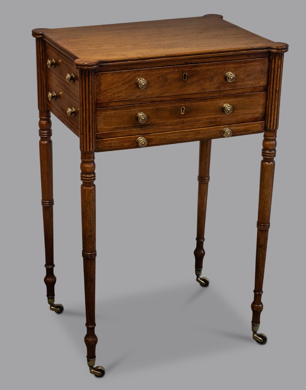A George III mahogany work table featuring two drawers with brass knobs, reeded corner columns, turned legs, and brass castors.