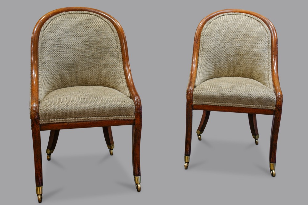 A pair of low-backed Regency mahogany slipper chairs featuring curved wooden frames, upholstered seats and backs, and sabre legs with brass castors. View II
