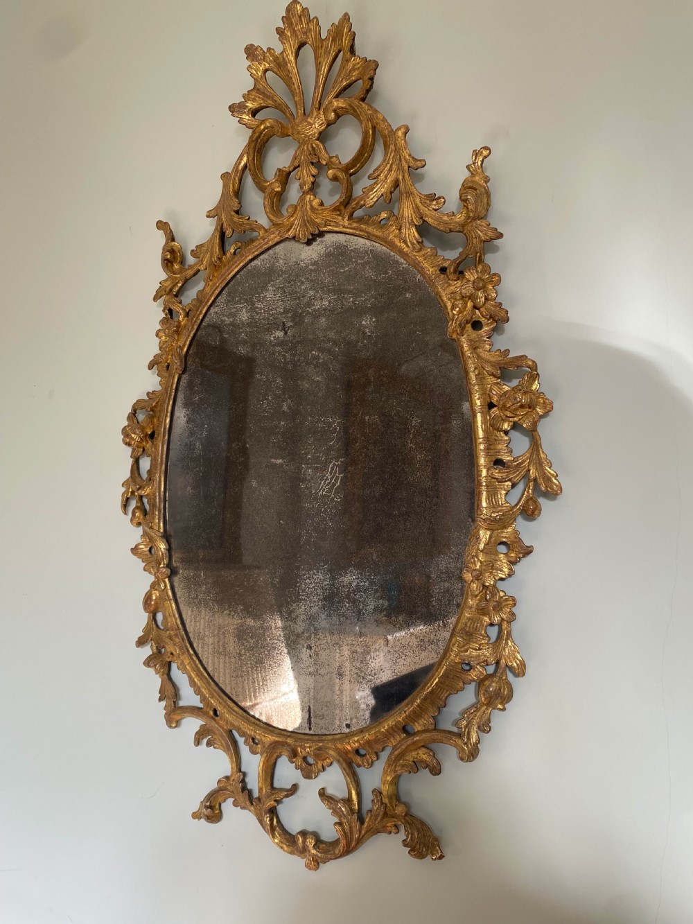 An oval George III carved giltwood wall mirror featuring pierced acanthus leaf cresting and scrollwork surrounding aged mirror glass.