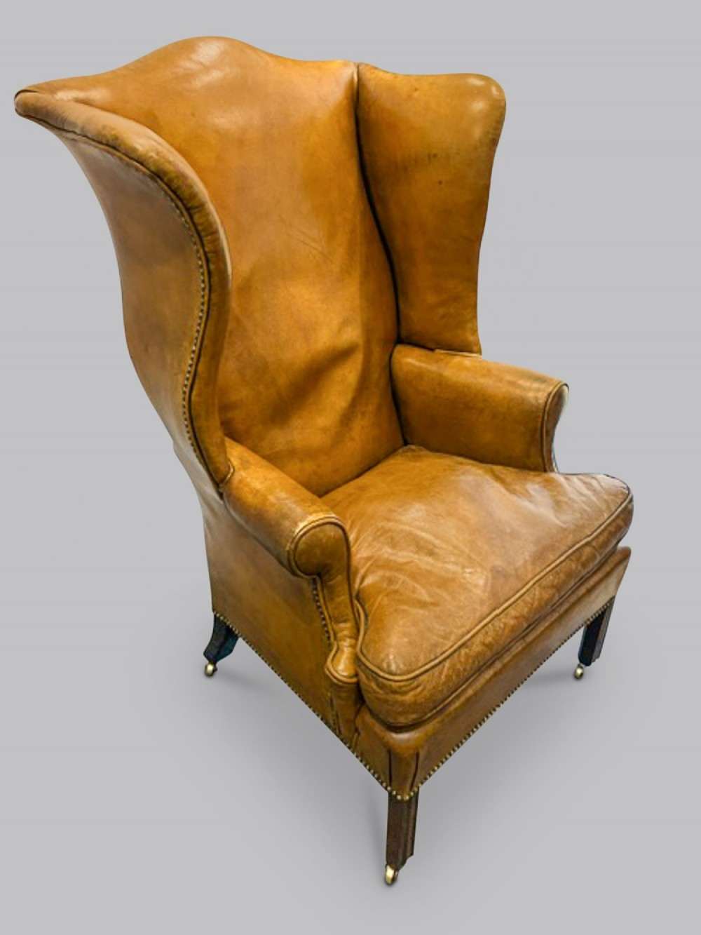 A George III wingback armchair upholstered in tan leather with brass stud detail along the seams and dark wood legs. View II