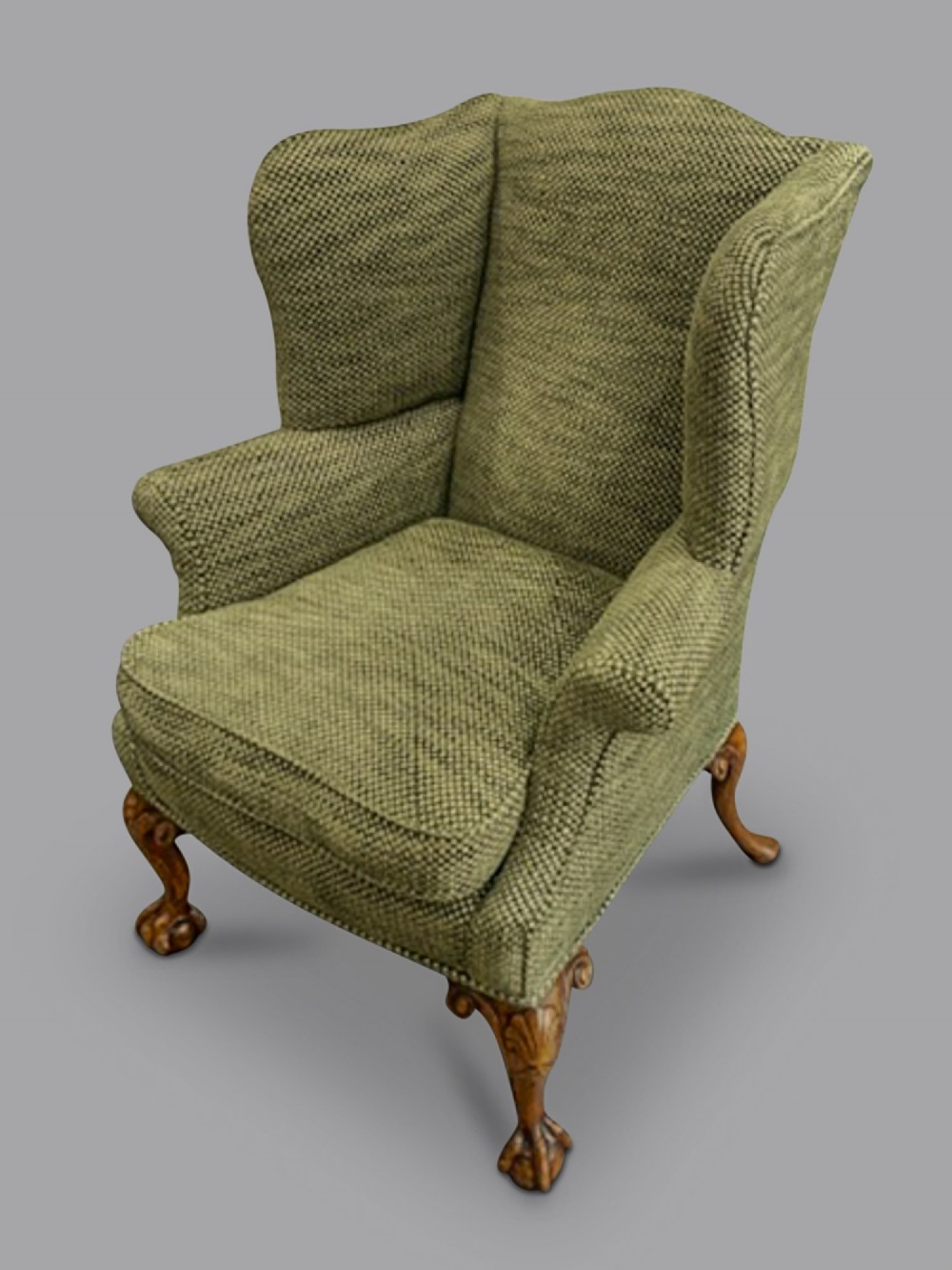 A mid-19th-century Victorian wingback armchair upholstered in textured green fabric with hand-carved walnut cabriole legs.