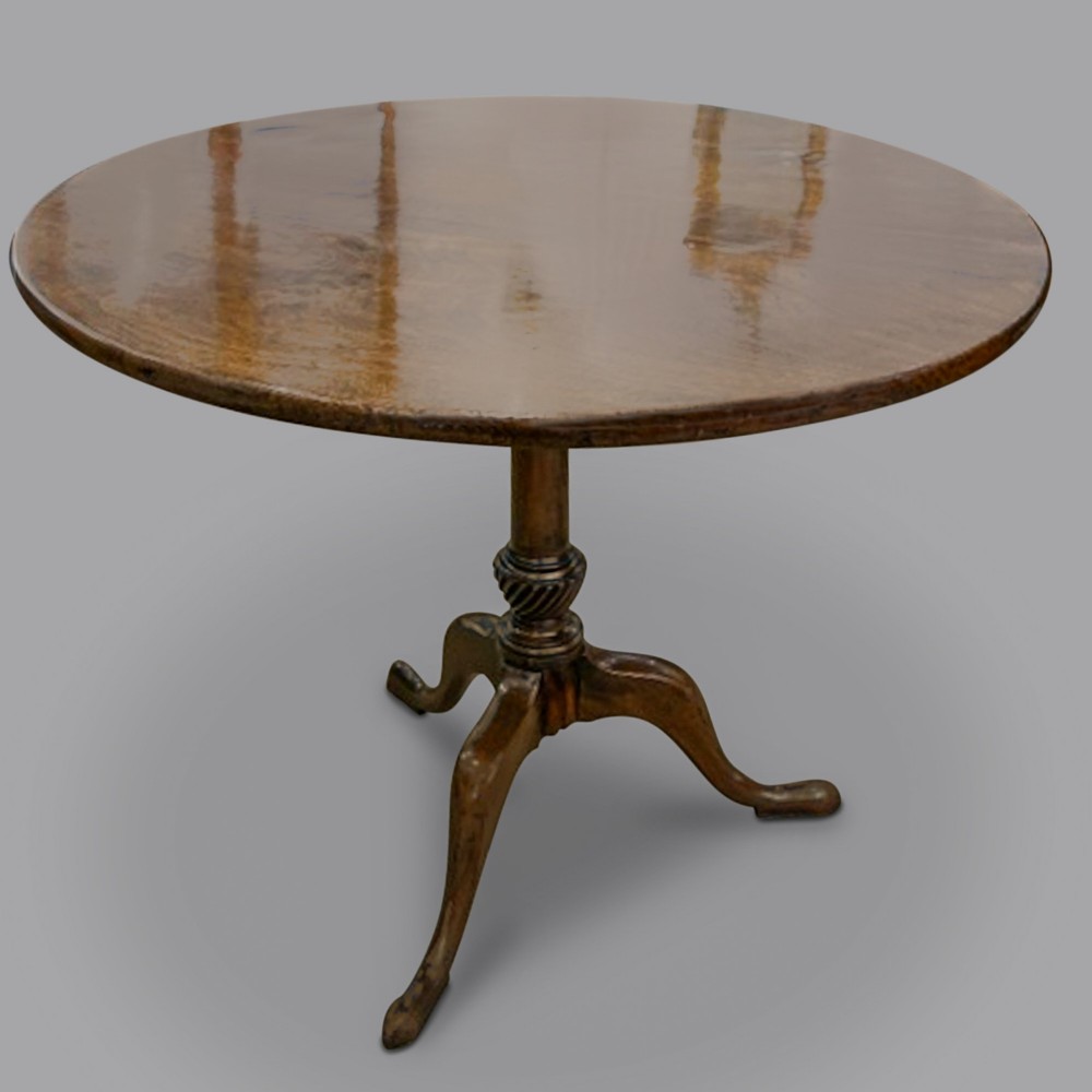 A George III mahogany tripod table featuring a circular top set on a central turned column with a spiral knop and three cabriole legs ending in pad feet.
