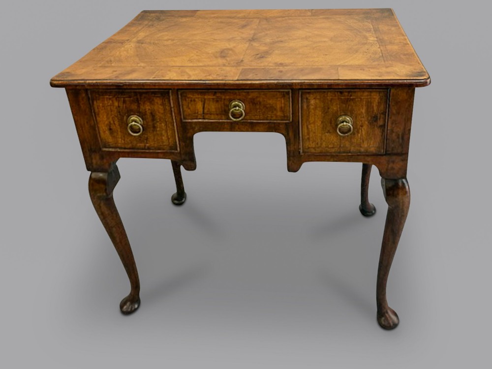 A George I walnut lowboy featuring three crossbanded drawers with brass drop ring handles, raised on four slender cabriole legs with pad feet.