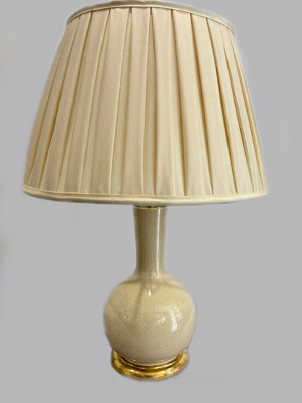 A late 19th-century French ceramic table lamp featuring a cream crackle glaze bulbous vase base on a gilded foot with a pleated silk shade.