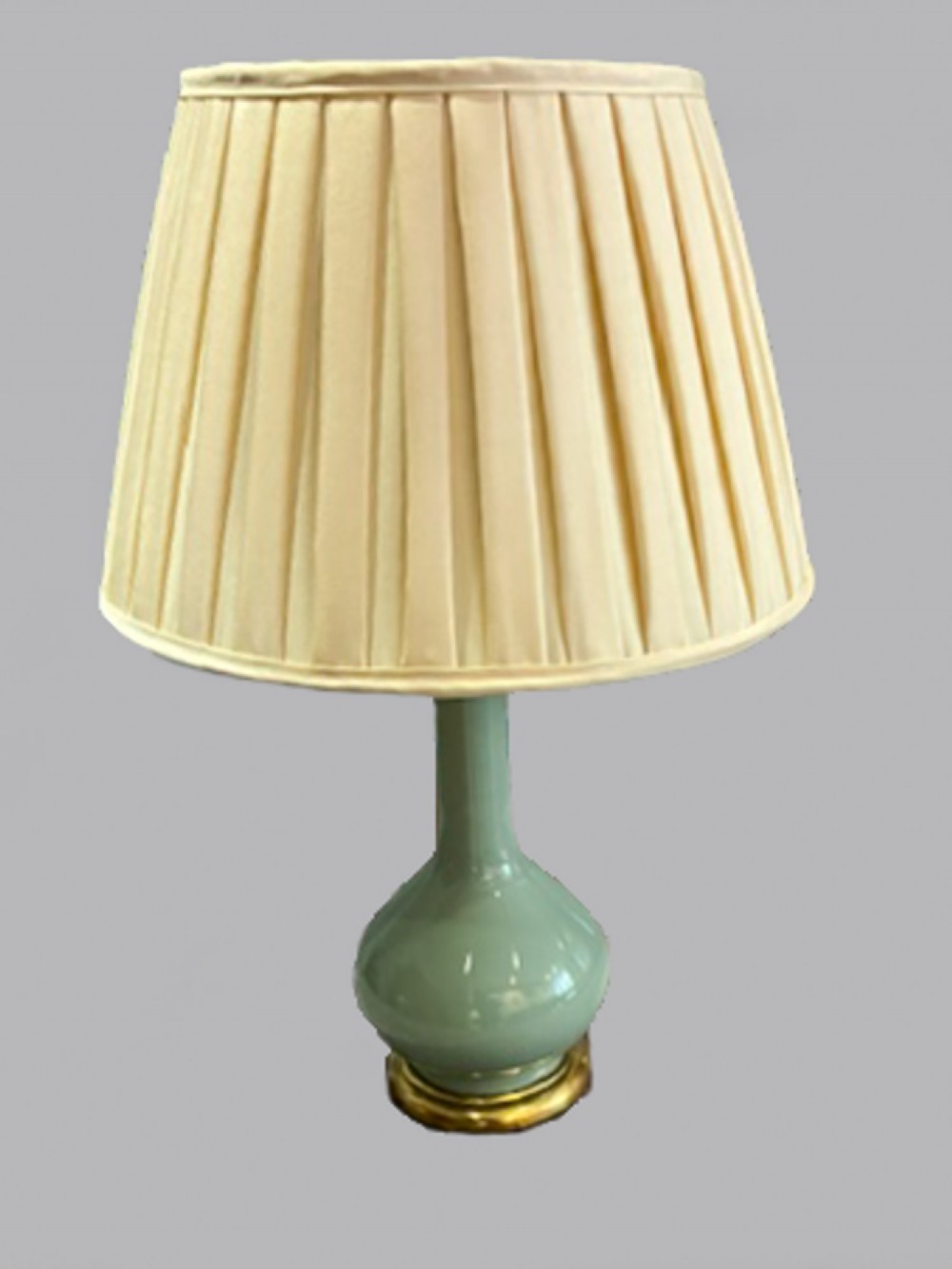 A 19th-century French celadon green ceramic table lamp featuring a rounded bottle-neck base mounted on brass with a cream pleated shade.