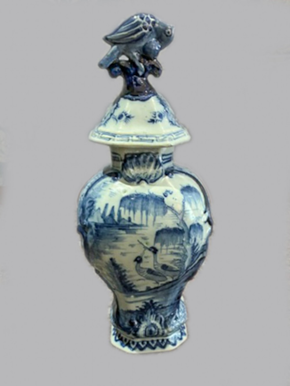 An 18th-century Dutch Delftware lidded vase decorated with blue and white hand-painted chinoiserie landscapes and topped with a sculpted bird finial.