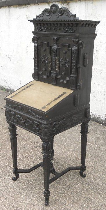 fig 1. A dark carved walnut ladies writing bureau cabinet featuring detailed carved cupboard doors, a slant-front writing slope, and turned legs with an H-stretcher.