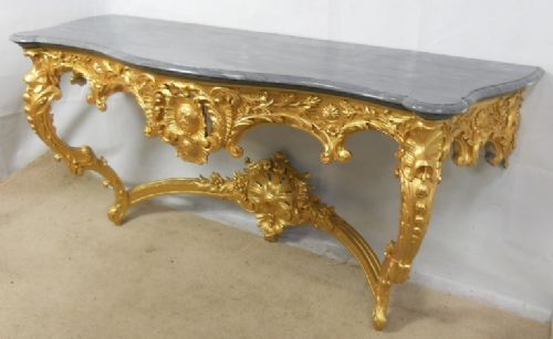 fig 1. An ornate French Rococo style giltwood console table featuring detailed carvings, cabriole legs, and a dark grey serpentine marble top.