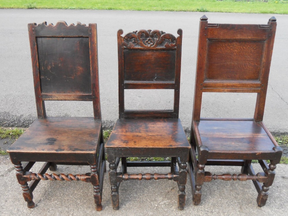 A set of three dark brown antique oak hall chairs featuring paneled backs, carved crest rails, solid wooden seats, and turned stretchers.