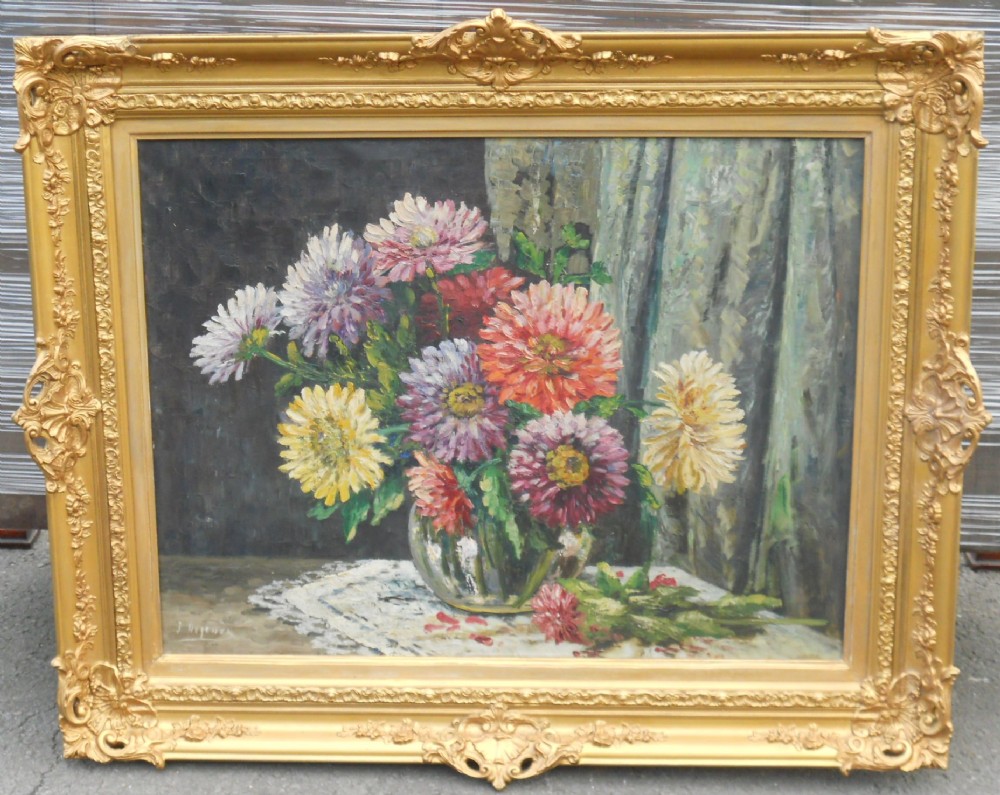 An oil painting depicting a bouquet of pink, yellow, and red dahlias in a clear glass vase, set within an ornate gilded swept frame.