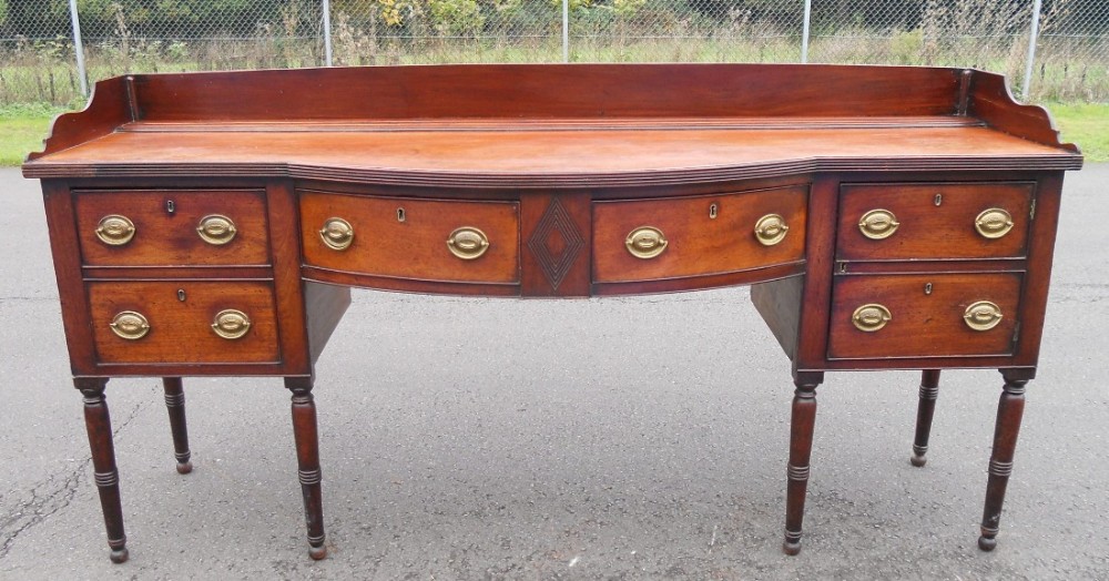 A Georgian mahogany bowfront sideboard featuring a raised gallery back, brass oval drop handles, and turned legs.