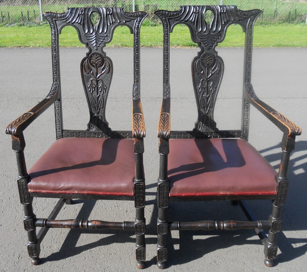 A pair of Victorian carved dark oak armchairs with high openwork backs, stylized floral splats, and padded brown leather seats.