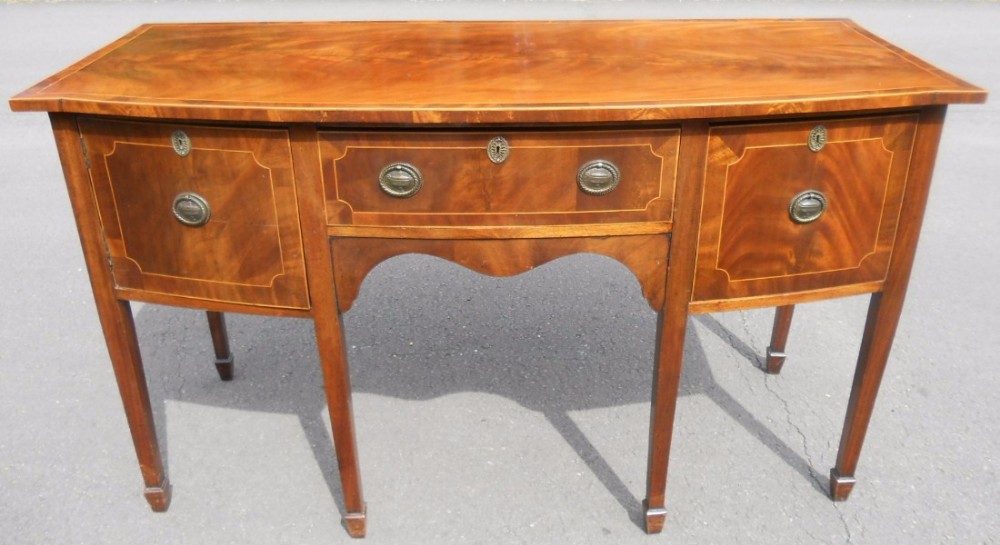 A Georgian inlaid mahogany bowfront sideboard featuring a convex curved front, central drawer over an arched apron, two side cupboards, and tapered square legs with spade feet.