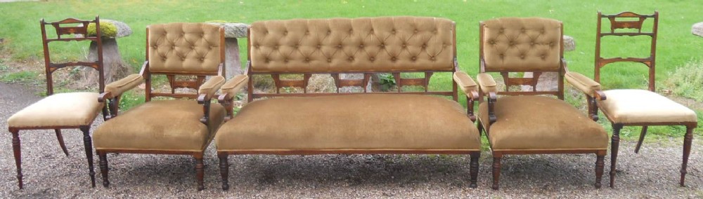 A five-piece Edwardian rosewood salon suite featuring a central button-back settee, two matching armchairs, and two side chairs with warm brown velvet upholstery.