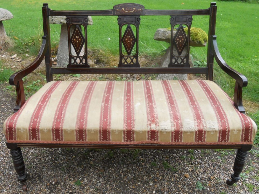 An Edwardian dark mahogany two-seater salon settee featuring inlaid back splats and a red and cream striped upholstered seat.