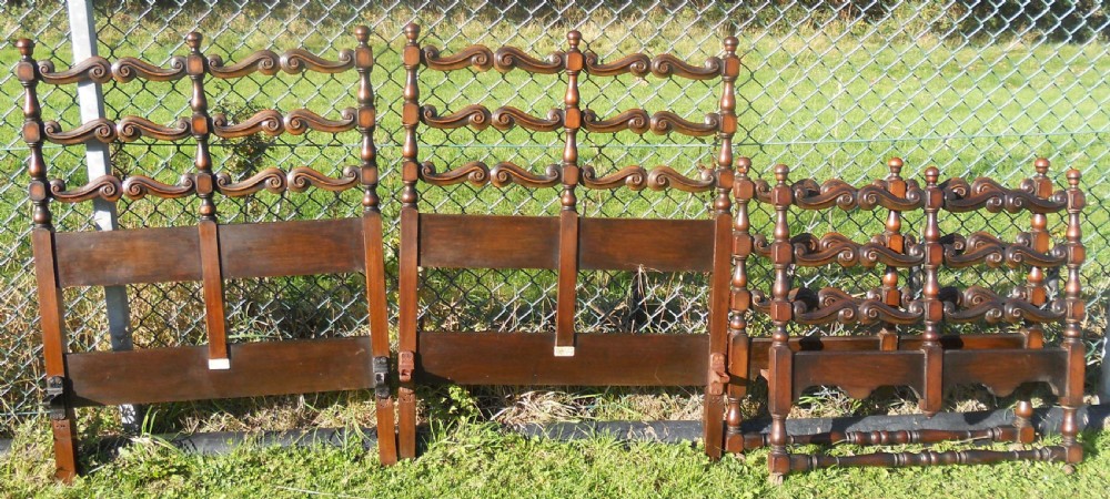 A pair of carved dark oak single bed frames displaying scroll-work horizontal rails, turned posts with finials, and solid lower panels.