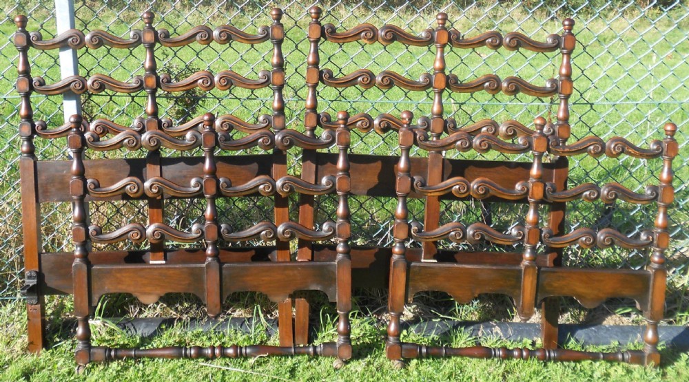 A pair of carved dark oak single bed frames displaying scroll-work horizontal rails, turned posts with finials, and solid lower panels. View II