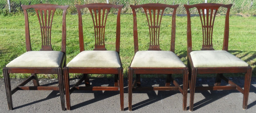 A set of four Georgian mahogany dining chairs featuring vertical pierced back splats, straight reeded front legs, and padded light-coloured seats.
