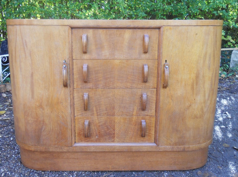 An Art Deco walnut sideboard featuring a central column of four drawers flanked by curved cupboard doors on a solid plinth base.