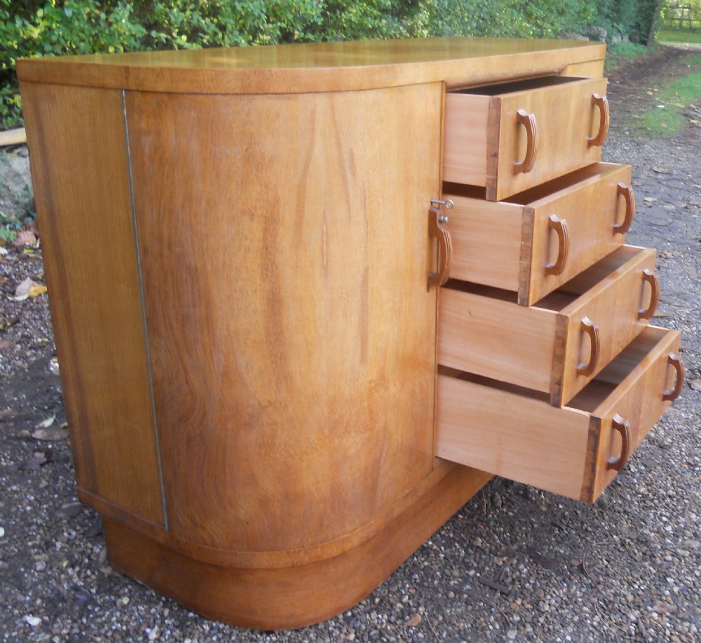 An Art Deco walnut sideboard featuring a central column of four drawers flanked by curved cupboard doors on a solid plinth base. View V