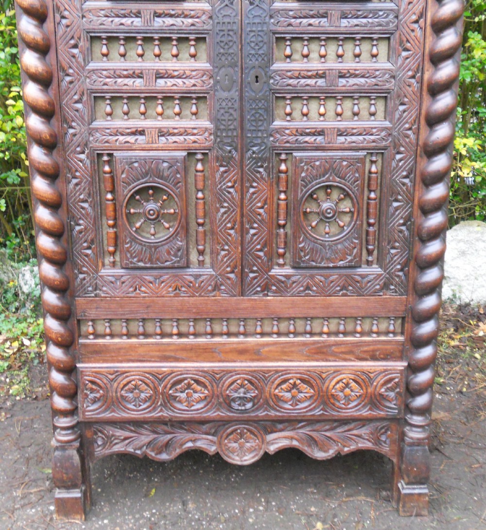 A dark carved oak Breton cupboard featuring barley twist corner columns, spindle galleries, and wheel relief panels. View VII