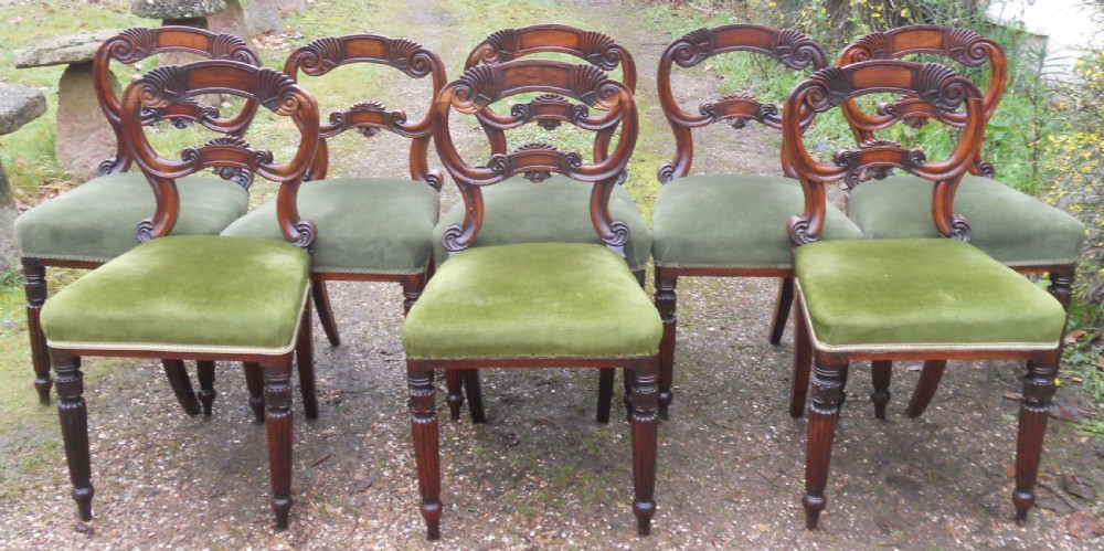 A set of eight dark rosewood Regency dining chairs featuring carved crest rails, turned front legs, and green velvet upholstered seats.