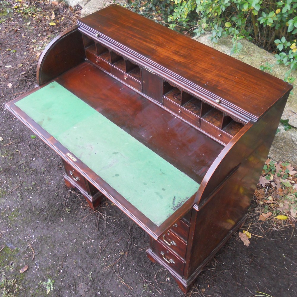 A small Georgian mahogany pedestal desk featuring a flexible slatted tambour rolltop cover, multiple drawers with brass swan-neck handles, and bracket feet. View IX