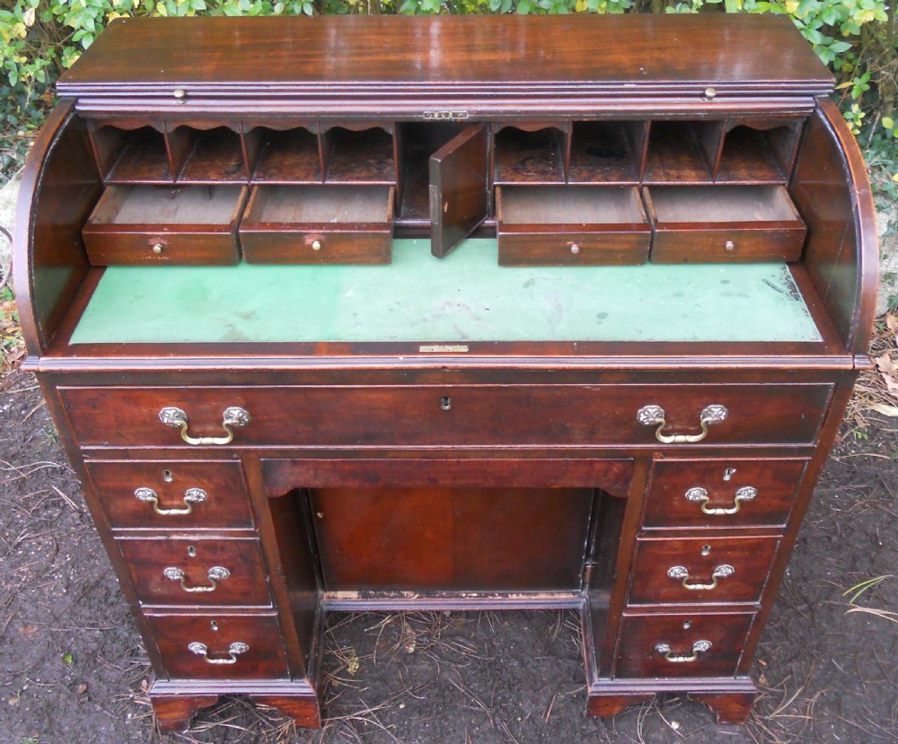 A small Georgian mahogany pedestal desk featuring a flexible slatted tambour rolltop cover, multiple drawers with brass swan-neck handles, and bracket feet. View X
