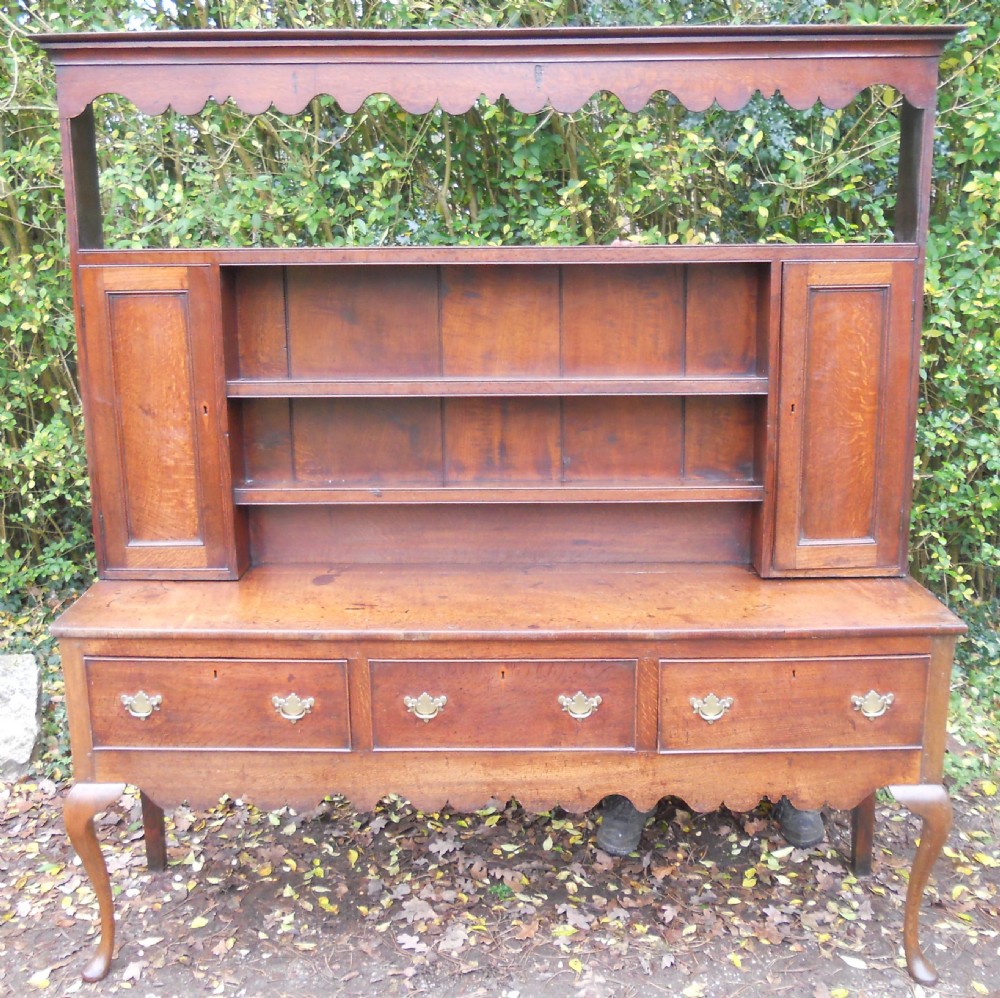A Georgian oak kitchen dresser featuring three base drawers, cabriole front legs, brass handles, and an upper rack with shelves flanked by cupboard doors. View III