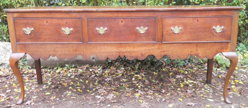 A Georgian oak kitchen dresser featuring three base drawers, cabriole front legs, brass handles, and an upper rack with shelves flanked by cupboard doors. View V
