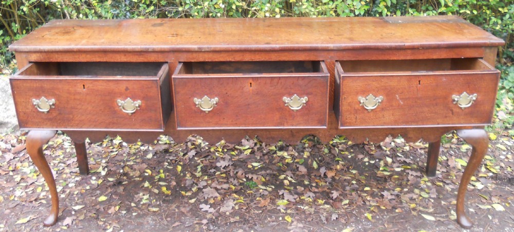A Georgian oak kitchen dresser featuring three base drawers, cabriole front legs, brass handles, and an upper rack with shelves flanked by cupboard doors. View IX