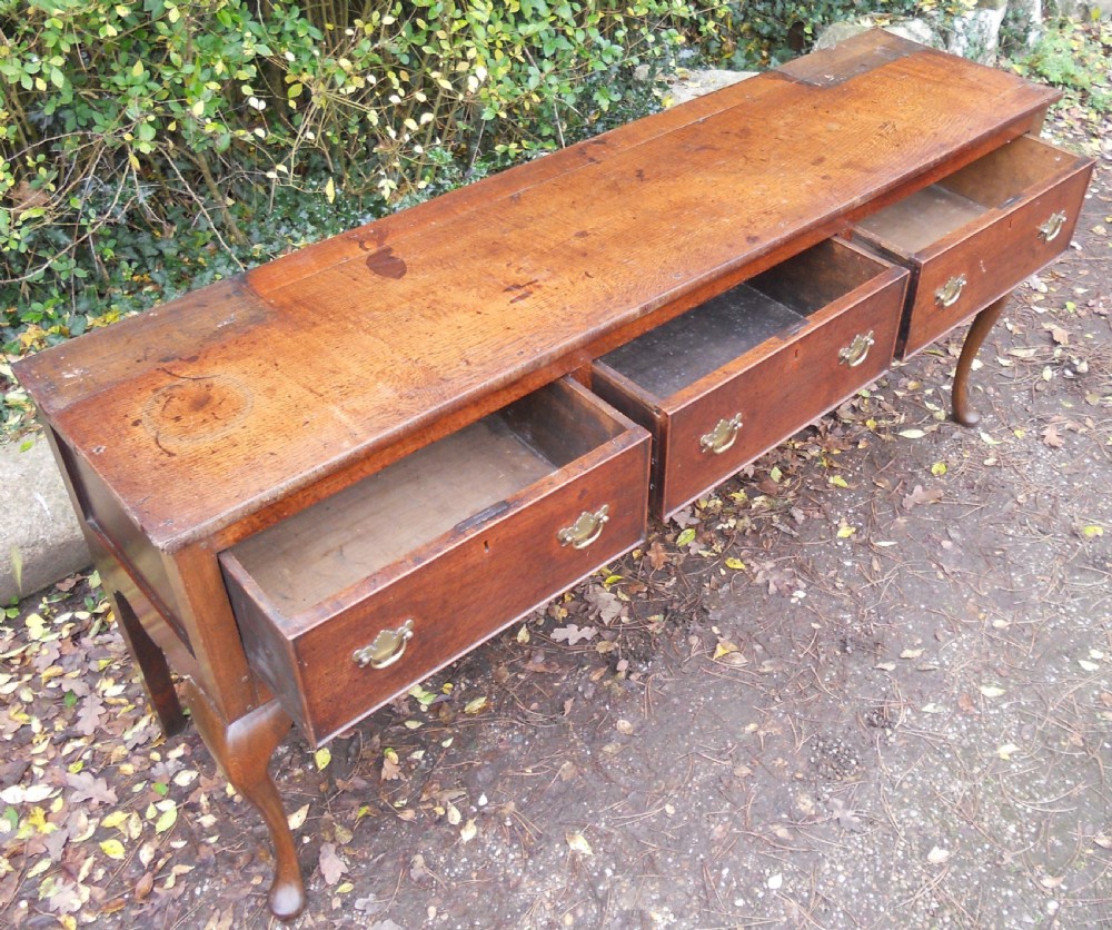 A Georgian oak kitchen dresser featuring three base drawers, cabriole front legs, brass handles, and an upper rack with shelves flanked by cupboard doors. View X