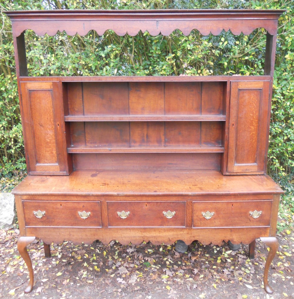 A Georgian oak kitchen dresser featuring three base drawers, cabriole front legs, brass handles, and an upper rack with shelves flanked by cupboard doors. View XII
