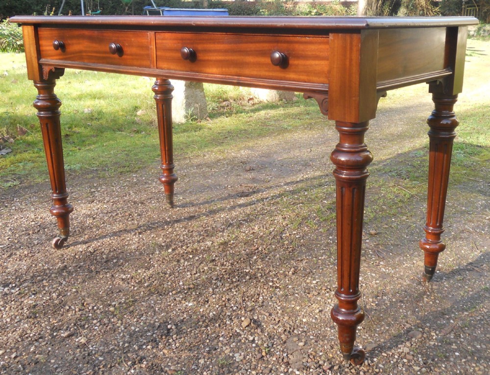 Victorian mahogany writing table featuring two frieze drawers with wooden knob handles, raised on turned and fluted legs with brass castors. View II