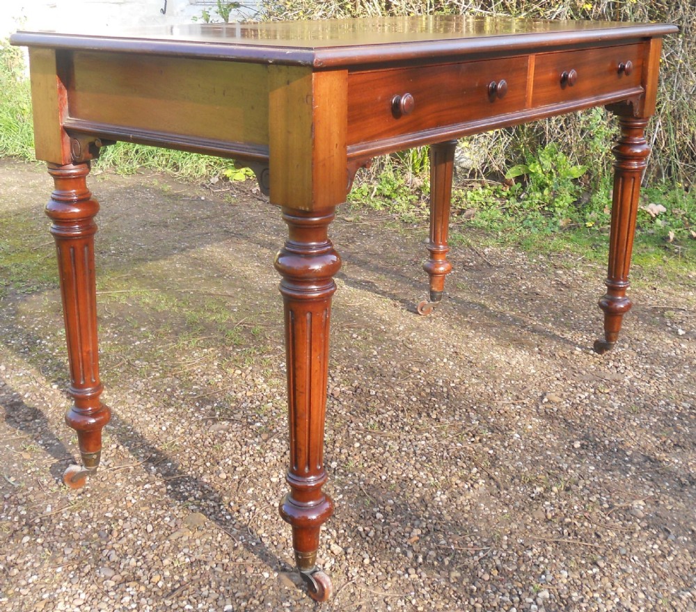 Victorian mahogany writing table featuring two frieze drawers with wooden knob handles, raised on turned and fluted legs with brass castors. View III