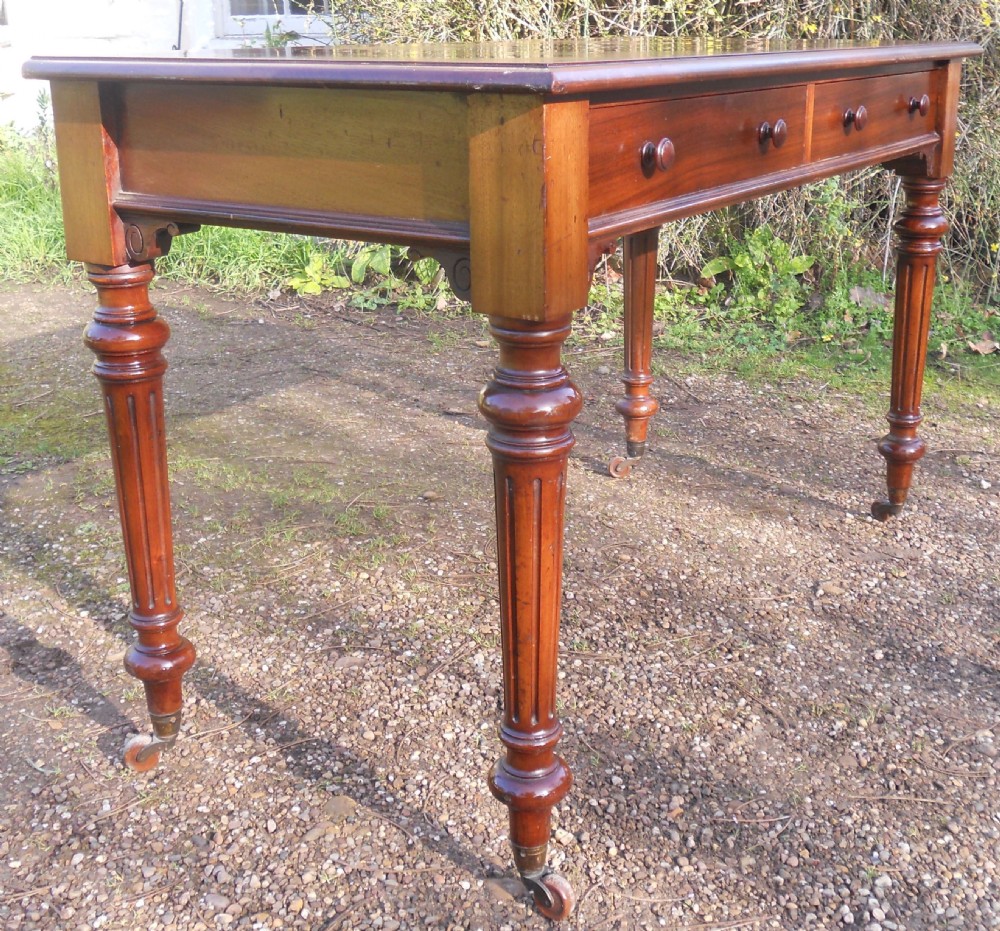 Victorian mahogany writing table featuring two frieze drawers with wooden knob handles, raised on turned and fluted legs with brass castors. View IV